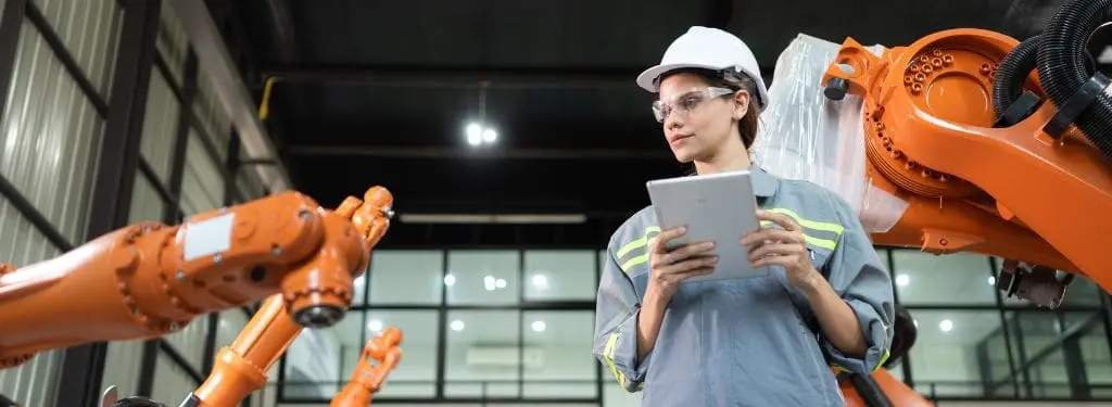 an engineer conducting maintenance on a manufacturing robot while accessing enterprise asset management software on a tablet device|eWorkOrders|IFS Ultimo|LLumin|MaintiMizer|TracOS