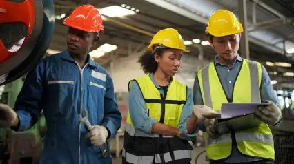 workers on a manufacturing site using a safety meeting sign in sheet on a laptop